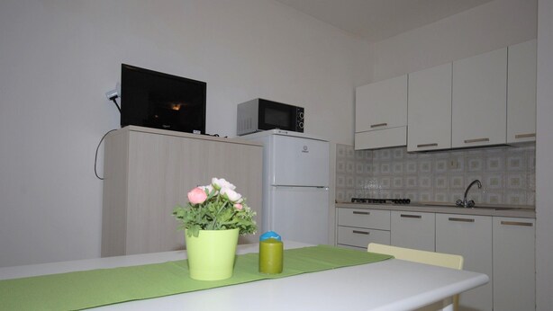 A small kitchenette with a microwave, a refrigerator, and a sink. There is a table with a green placemat and a vase with flowers. - The perfect cozy studio stay by Beahost Rentals (Lignano Sabbiadoro)