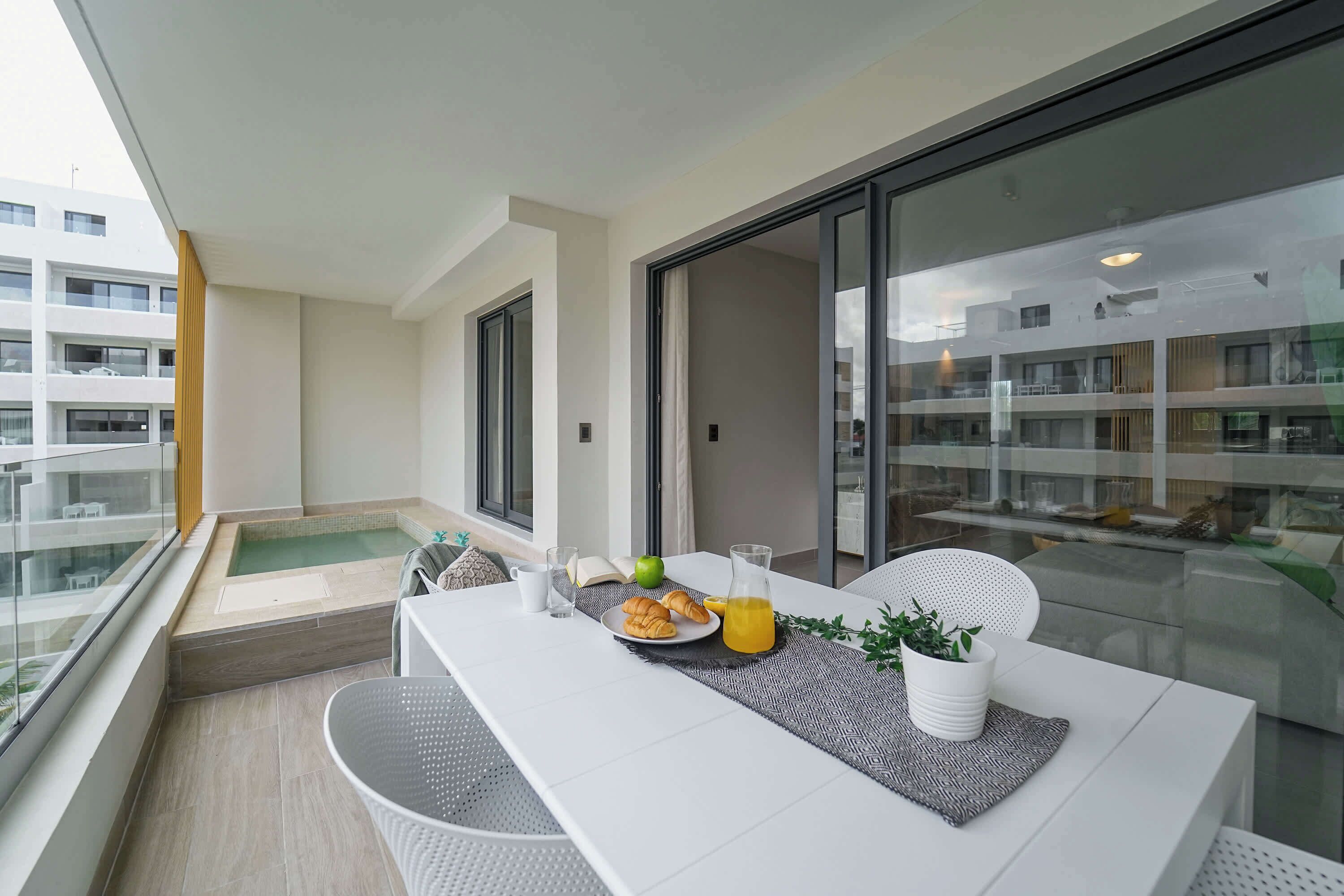 Un balcón con una mesa dispuesta para el desayuno, que incluye croissants, una manzana y una jarra de jugo.