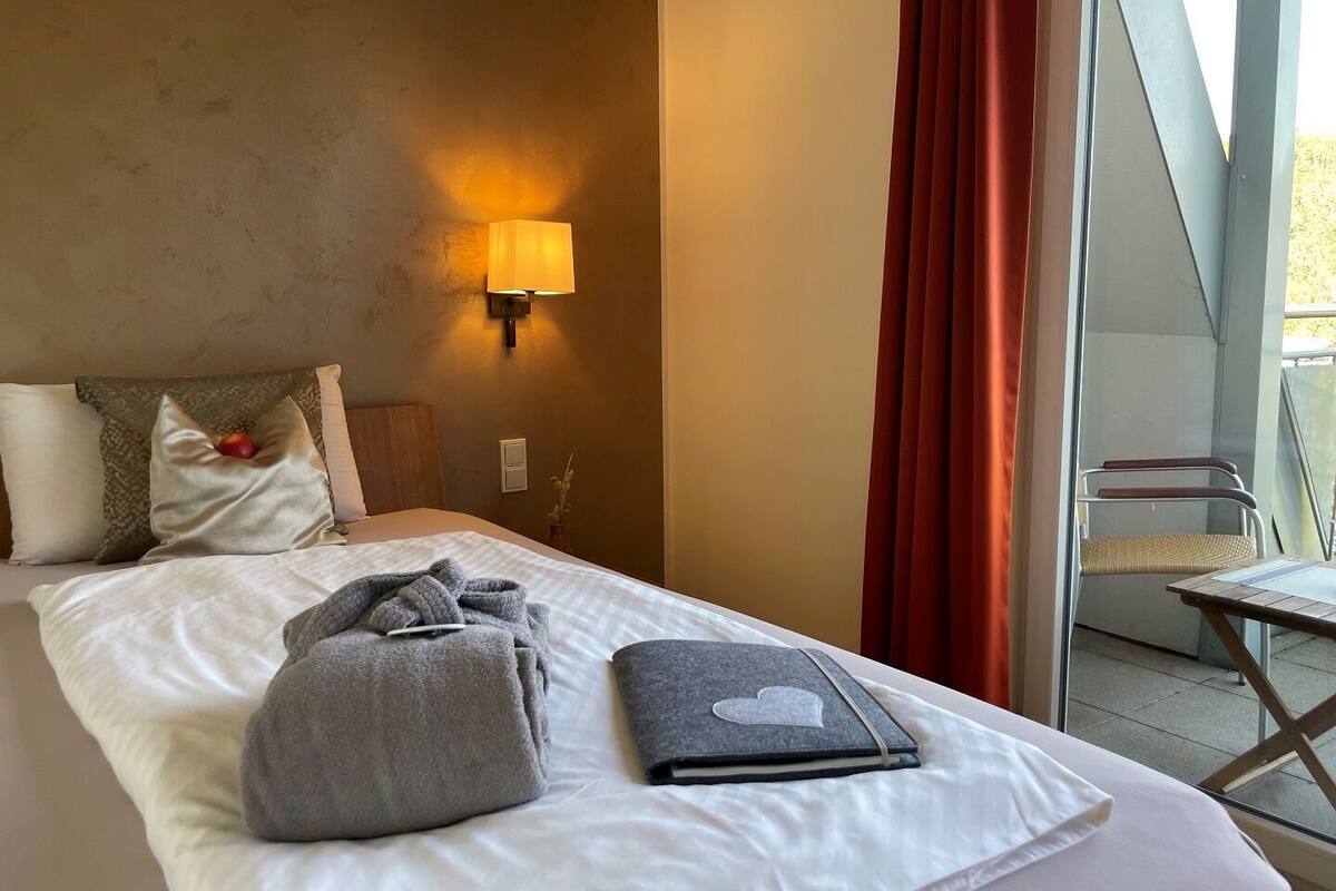 A hotel room with a bed, a bedside lamp, a window with curtains, and a chair by the window.