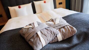 A neatly made bed with a dark gray bedspread and two towels tied with a brown and white striped towel.