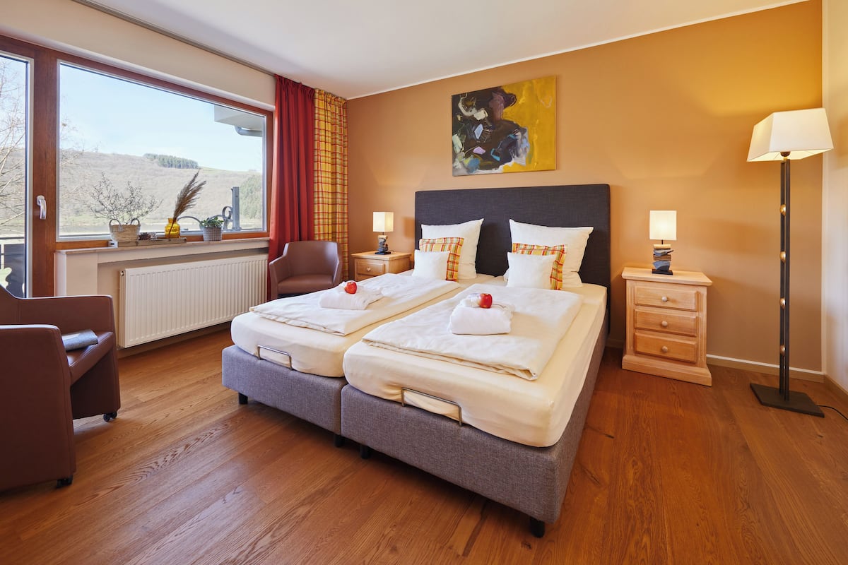 A double bed with two pillows, a nightstand, a chair, a floor lamp, and a window with a view of the outdoors.