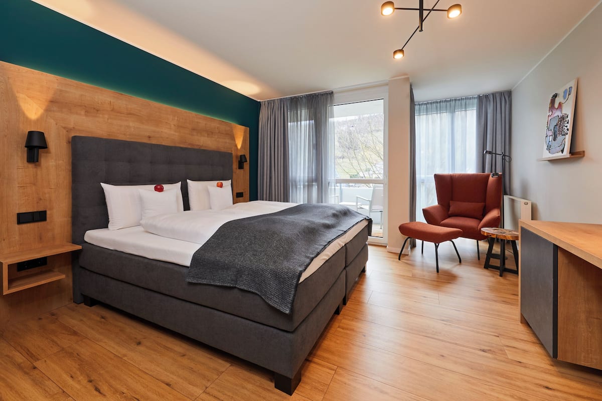 A modern hotel room with a large bed, a wooden headboard, a desk, and a chair.