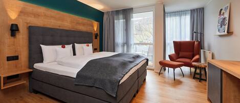 Una habitación de hotel moderna con una cama grande, cabecera de madera, escritorio y una silla.