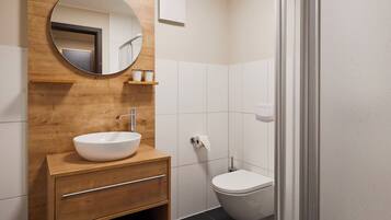 A modern bathroom with a wooden vanity, a round mirror, a white sink, a toilet, and a glass shower enclosure.
