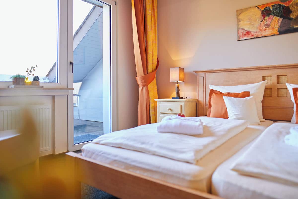 A hotel room with a bed, a nightstand with a lamp, a window with curtains, and a painting on the wall.