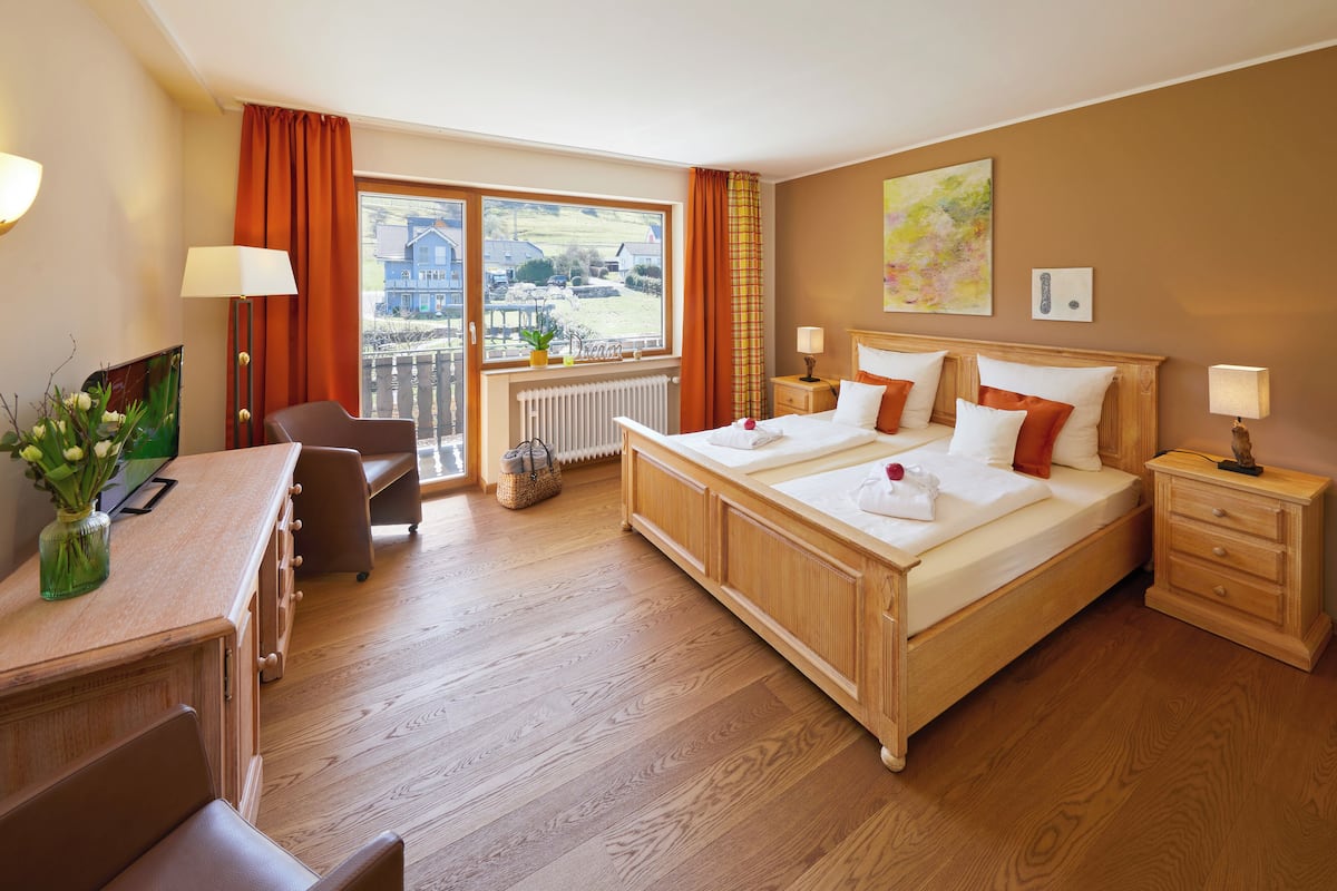 A hotel room with a large bed, a desk, a chair, and a view of the outside.