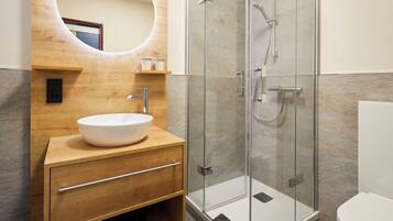 Un baño moderno con tocador de madera, un espejo grande, ducha con cerramiento de vidrio y un inodoro blanco.