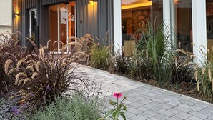 A modern building with a covered entrance, a paved walkway, and various plants and flowers. - NaturPur Hotel Maarblick (Meerfeld)
