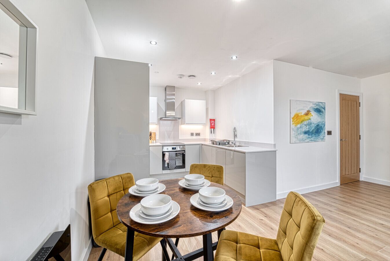 A modern kitchen with white cabinets, a central island, and a dining area with yellow chairs and a wooden table.