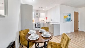 Une cuisine moderne avec des meubles blancs, un îlot central et un coin repas agrémenté de chaises jaunes et d’une table en bois.