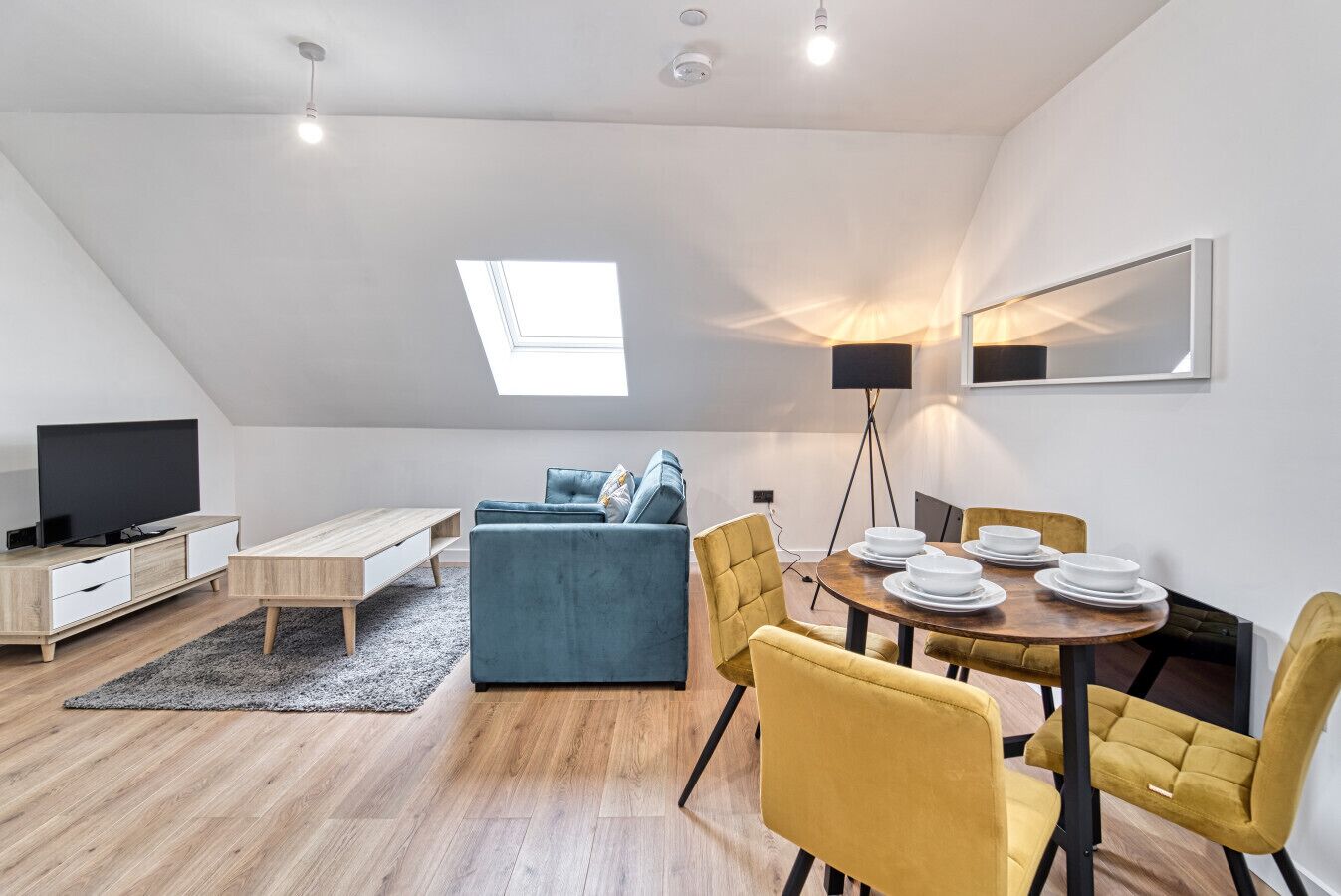 A modern loft apartment with a dining area, a sofa, a TV, and a skylight.