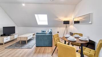 A modern loft apartment with a dining area, a sofa, a TV, and a skylight.