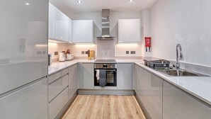 Une cuisine moderne dotée d’appareils électroménagers en acier inoxydable, d’un plancher en bois et de meubles de rangement blancs.