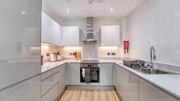 A modern kitchen with stainless steel appliances, a wooden floor, and white cabinetry.
