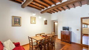 A dining area with a wooden table and chairs, a red sofa, and a television in the corner.