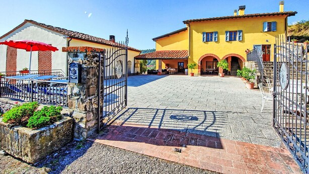 A courtyard with a yellow building, a red umbrella, and a stone gate. - Beautiful apartment for 4 people with WIFI, pool, A/C, TV, pets allowed and panoramic view (Pontassieve)
