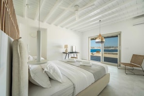 Relax in a serene coastal retreat with a large bed, wicker chair, and stunning sea views.