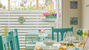 A dining area with a table set for four, chairs, a small table with a vase of flowers, and a wooden fence with plants behind. - Cosy Retreat in Galway City Centre (Galway)