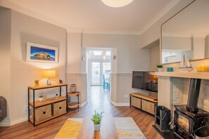 Una sala de estar moderna con chimenea, suelo de madera, televisor y vistas al exterior a través de un ventanal.