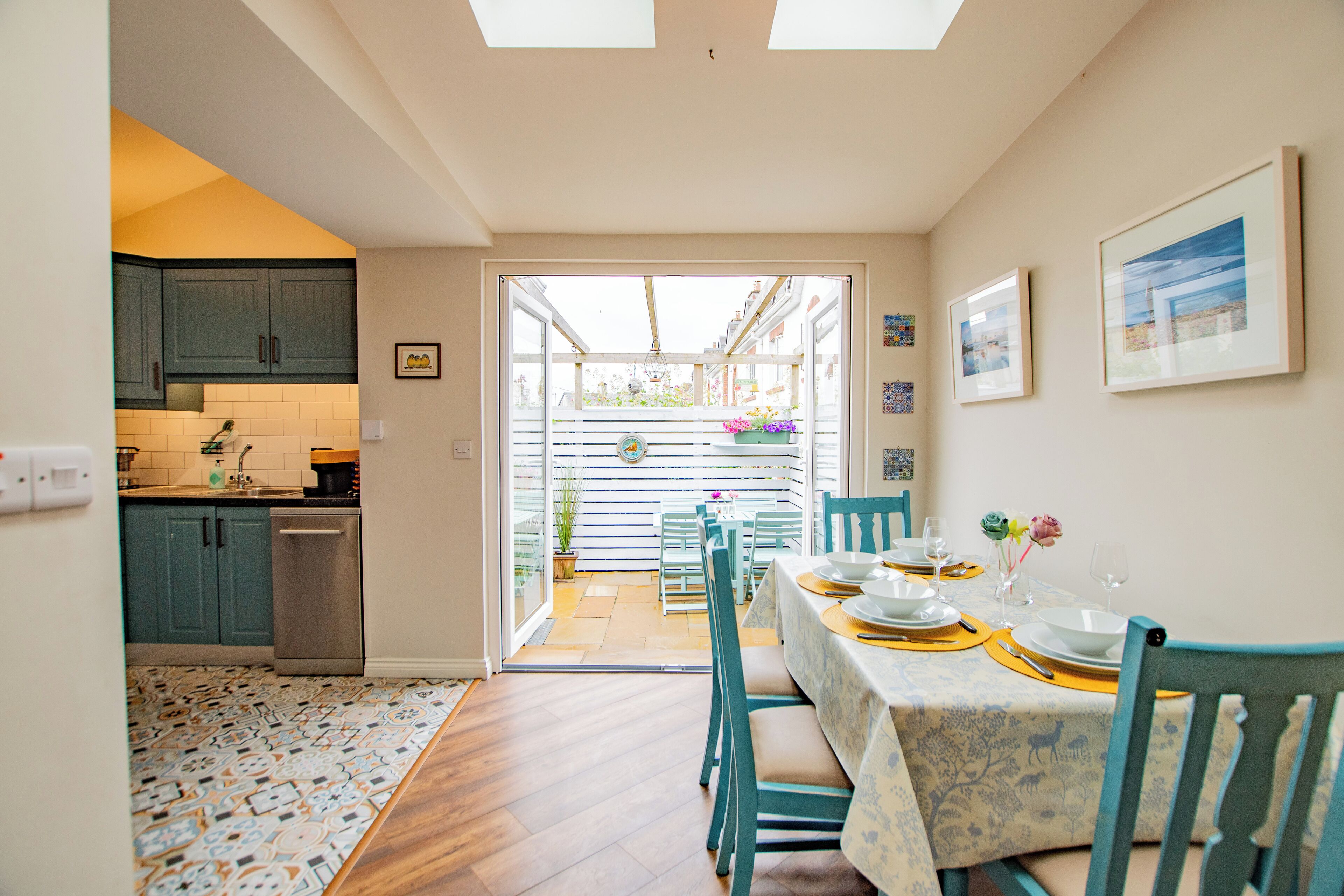 Un coin repas avec une table dressée pour quatre personnes, une cuisine en arrière-plan et, à travers une porte vitrée, une vue sur un balcon extérieur.