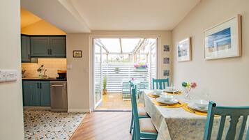 Un coin repas avec une table dressée pour quatre personnes, une cuisine en arrière-plan et, à travers une porte vitrée, une vue sur un balcon extérieur.