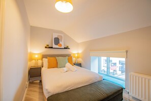 Quarto de hotel com uma cama grande, duas luminárias de cabeceira, uma janela com vista e uma luz no teto.