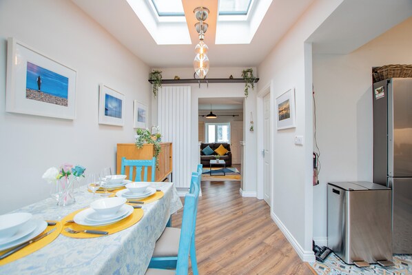 Una cocina moderna con refrigerador empotrado, un comedor con una mesa larga dispuesta para cuatro personas, y un pasillo que conduce a una sala de estar.