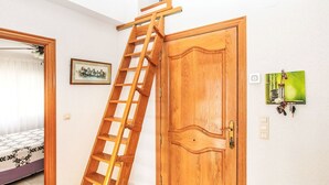 Una habitación con puerta de madera, una escalera, un cuadro enmarco y un atril para llaves en la pared.