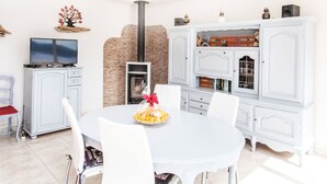 Una sala de estar moderna con una mesa de comedor blanca, sillas blancas, una chimenea, un televisor y una estantería.