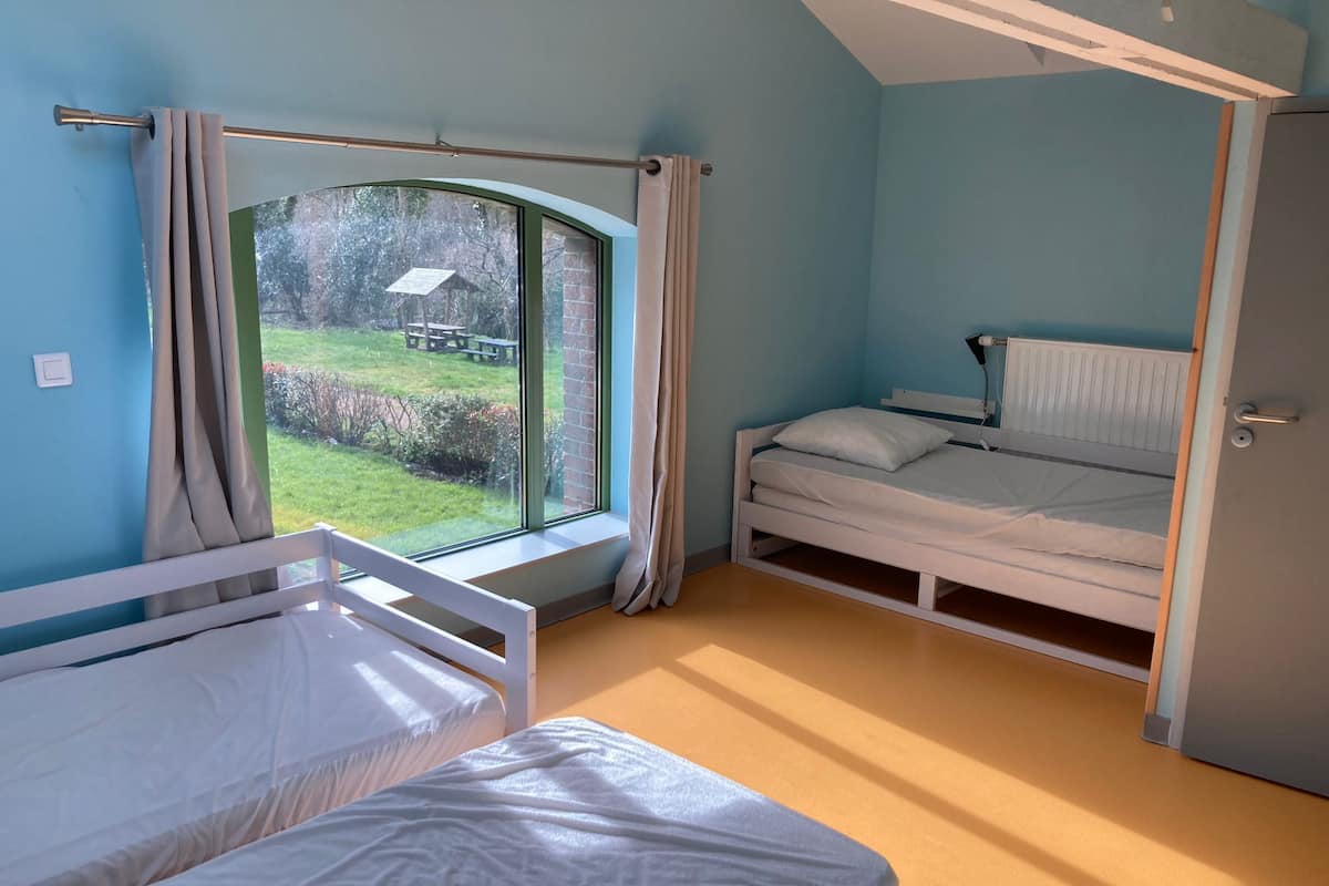 Una camera da letto con un letto singolo, una finestra con tende, un termosifone e una porta.