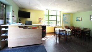 A classroom with a wooden desk, chairs, a television, and a window. - Ostal Scrignac - Gîte d'étape de la Gare (Scrignac)