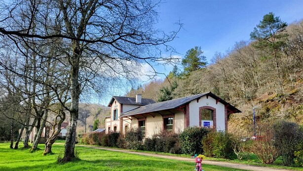 A two-story house with a sloped roof, surrounded by a grassy area and trees. - Ostal Scrignac - Gîte d'étape de la Gare (Scrignac)