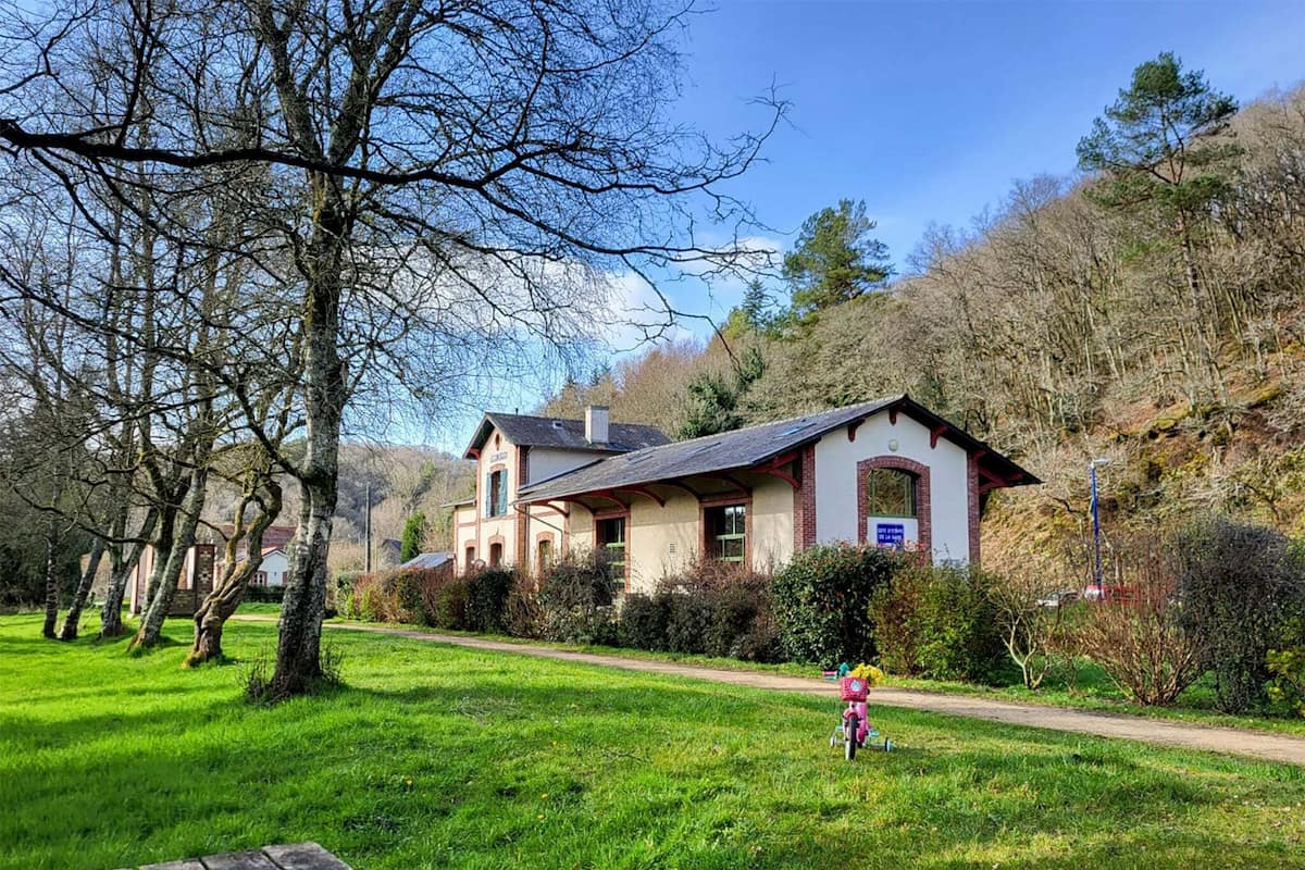 Una casa a due piani con tetto spiovente, circondata da un prato e alberi.