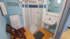 A bathroom with a glass shower enclosure, a sink, a mirror, and a wooden chair. - Ostal Scrignac - Gîte d'étape de la Gare (Scrignac)