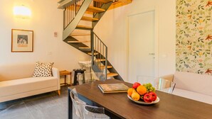 A modern living room with a wooden staircase, a dining table with fruit, a white sofa, and a floral wallpaper. - Beautiful apartment for 4 people with WIFI, pool, A/C, TV, patio and panoramic view (Dervio)