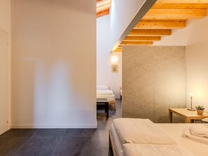 A modern hotel room with a large bed, a small bedside table with a lamp, and a view of the adjacent room. - Cosy apartment for 4 people with WIFI, A/C, pool, TV and patio (Dervio)