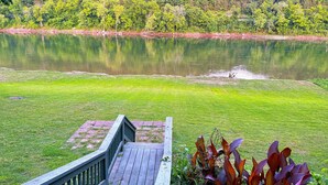 Ein grasbewachsenes Gelände mit einer Holzterrasse, die zu einem See führt, umgeben von dichtem Wald.