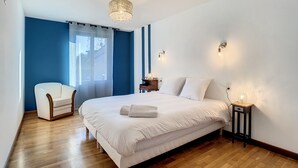 A bedroom with a large bed, a chair, a nightstand, and a chandelier. - Gîte Le Karrdi (10 pers) in Brittany, ideal for families. Pets welcome! (Landavran)