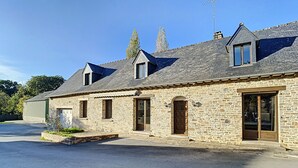 A stone building with a sloped roof, multiple windows, and a large garage door. - Gîte Le Karrdi (10 pers) in Brittany, ideal for families. Pets welcome! (Landavran)