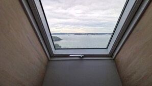 Une lucarne offrant une vue sur une étendue d’eau et sur la terre ferme, qui se trouve au loin.