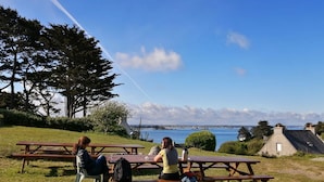 Deux tables de pique-nique, avec des personnes assises autour, offrent une vue sur une étendue d’eau et une côte lointaine.