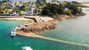 Une ville côtière dotée d’une digue rocheuse, d’eaux turquoise et limpides, et de maisons qui bordent la côte.