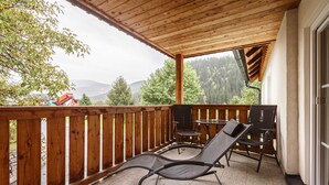 Una terraza de madera con dos sillas reclinables y una mesita, con vistas a un paisaje montañoso.