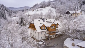 Un edificio de madera de varios pisos con techo cubierto de nieve, rodeado de árboles y un paisaje montañoso.
