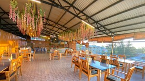 Un restaurante espacioso con mesas y sillas de madera, decoraciones florales colgantes y vistas a edificios.