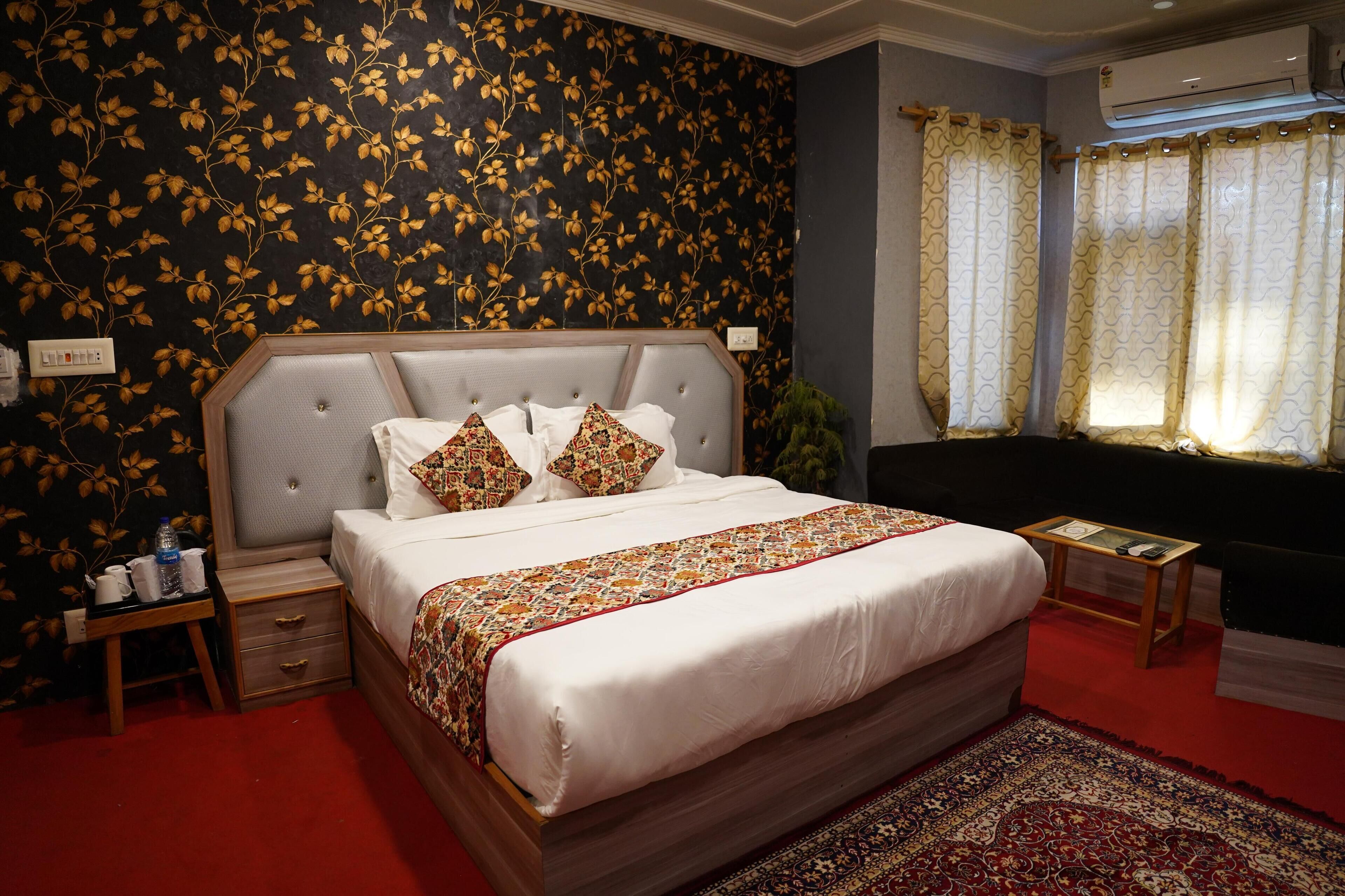 A bedroom with a large bed, a nightstand, a bedside table, a window with curtains, and a wall with a floral pattern.