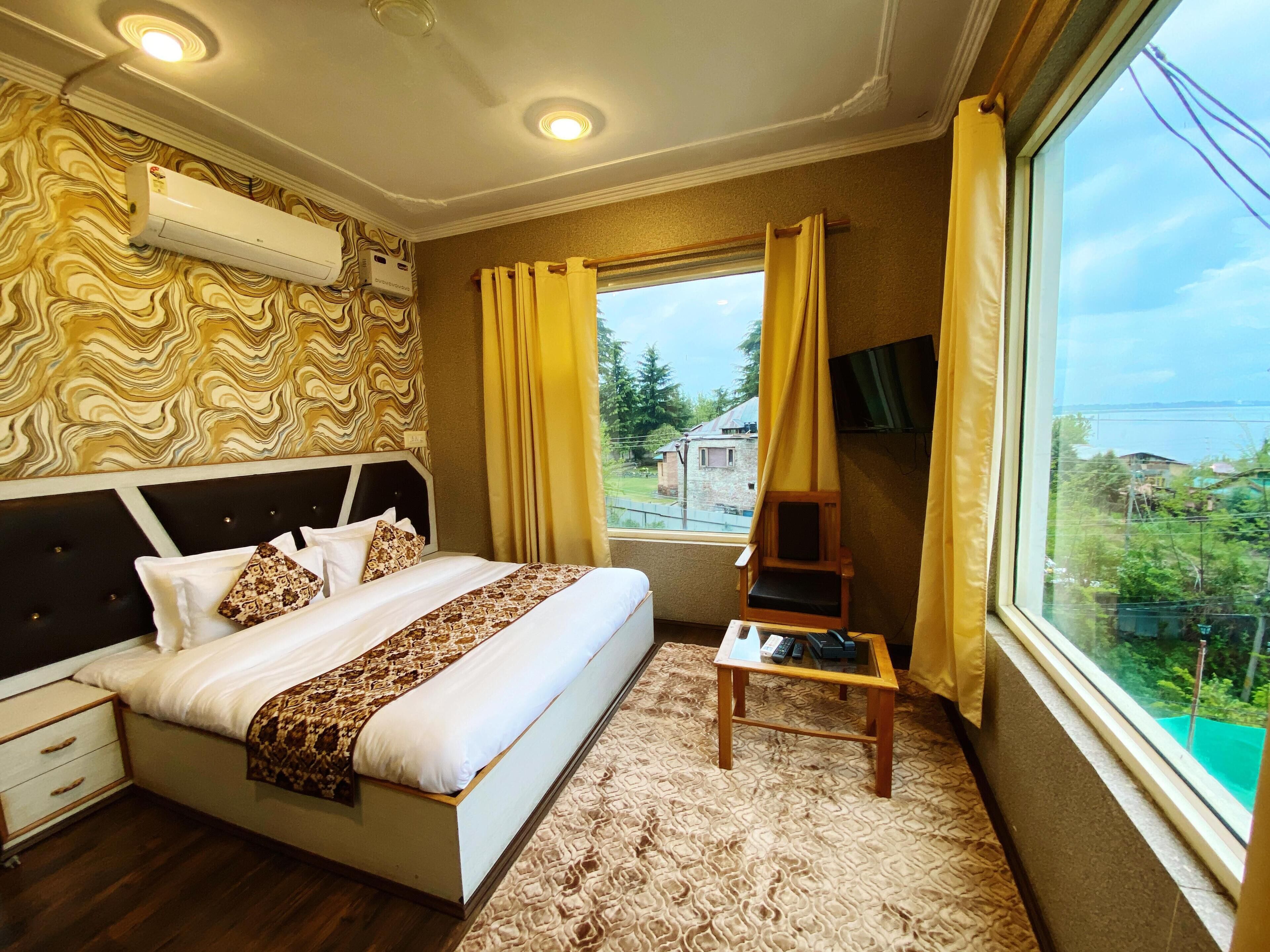 Un dormitorio con una cama grande, una mesita de noche, una silla, un televisor y una ventana con cortinas.