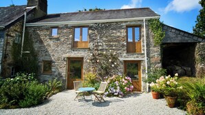 Une maison en pierre avec une allée en gravier, des portes en bois et un petit patio avec une table et des chaises.