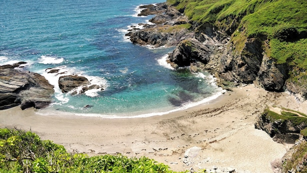 Un paysage côtier caractérisé par une plage de sable, des falaises rocheuses et une eau d’un bleu limpide.