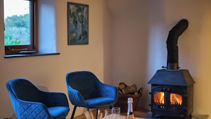 Une pièce chaleureuse avec deux fauteuils bleus, une table en bois sur laquelle se trouvent une bouteille et des verres, et un poêle à bois.